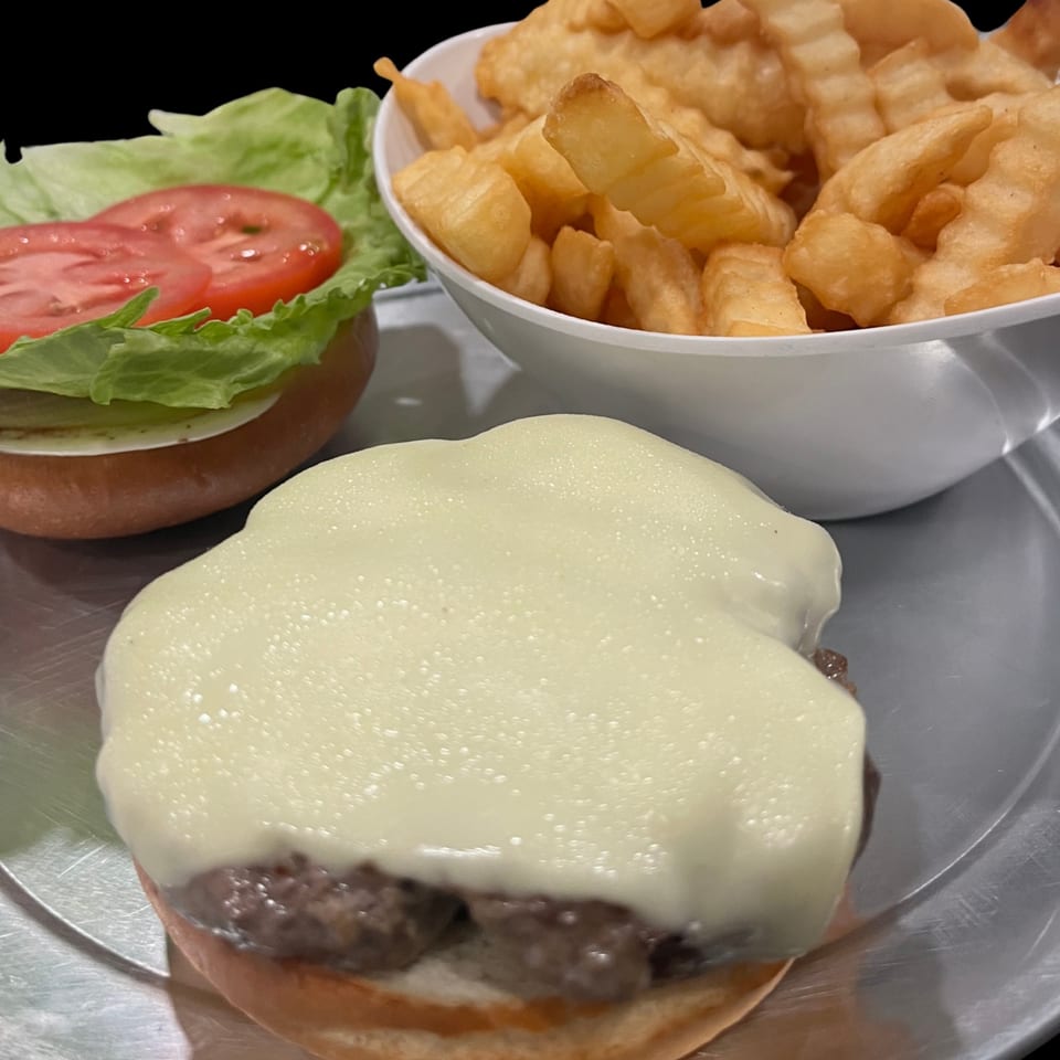 Cheeseburger with melted cheese, lettuce, tomato, and a side of crinkle-cut fries.