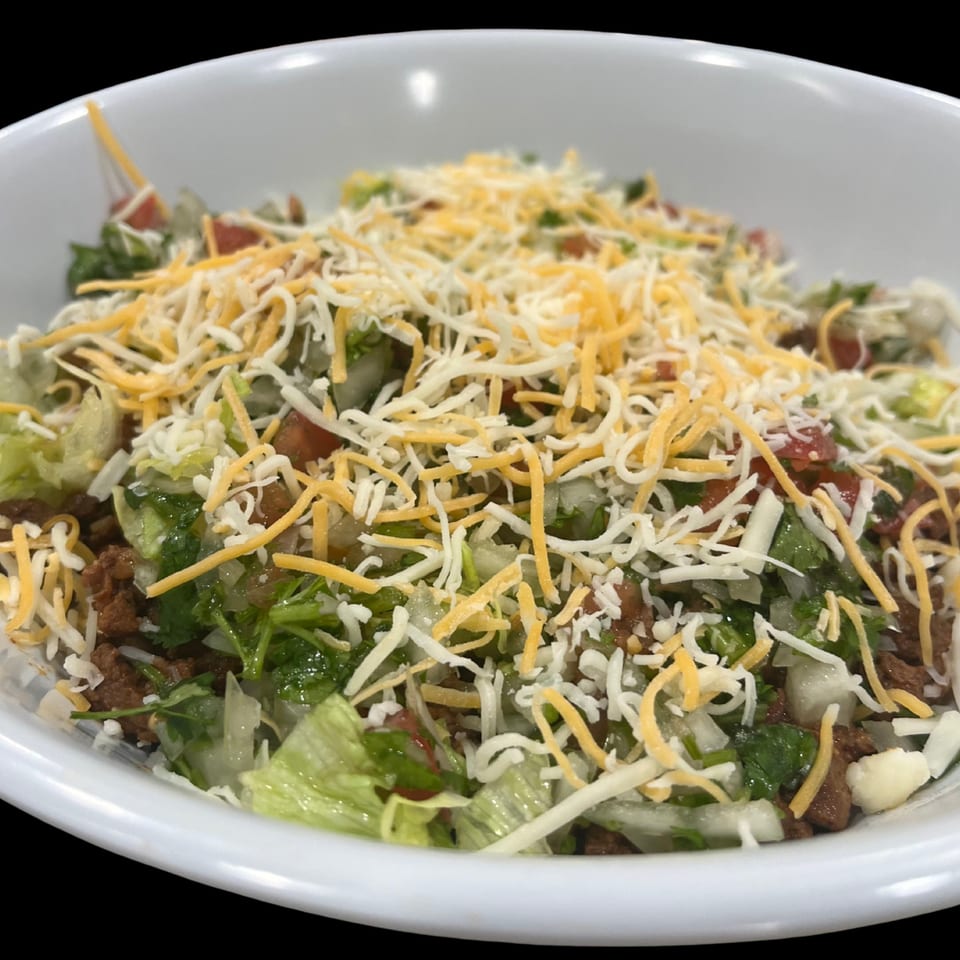 A close-up of a Family Grill taco salad with ground beef, lettuce, tomatoes, and shredded cheese.