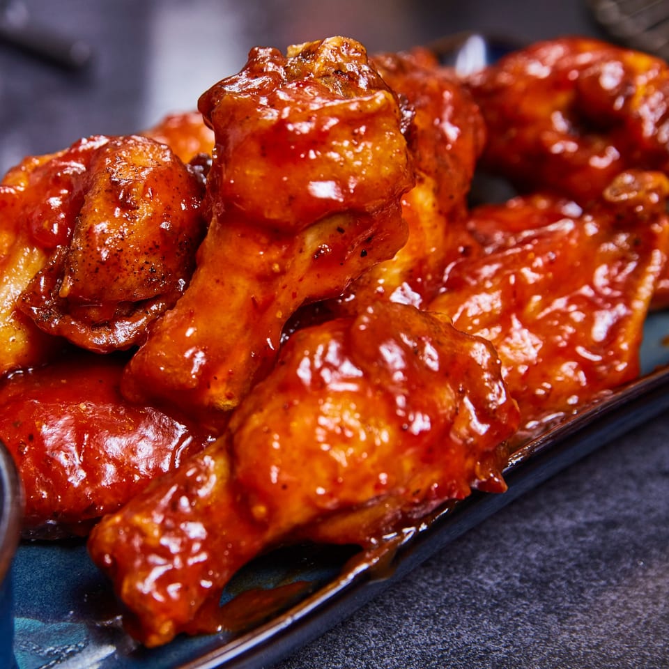 Close-up of several spicy, saucy chicken wings on a blue plate from Family Grill.