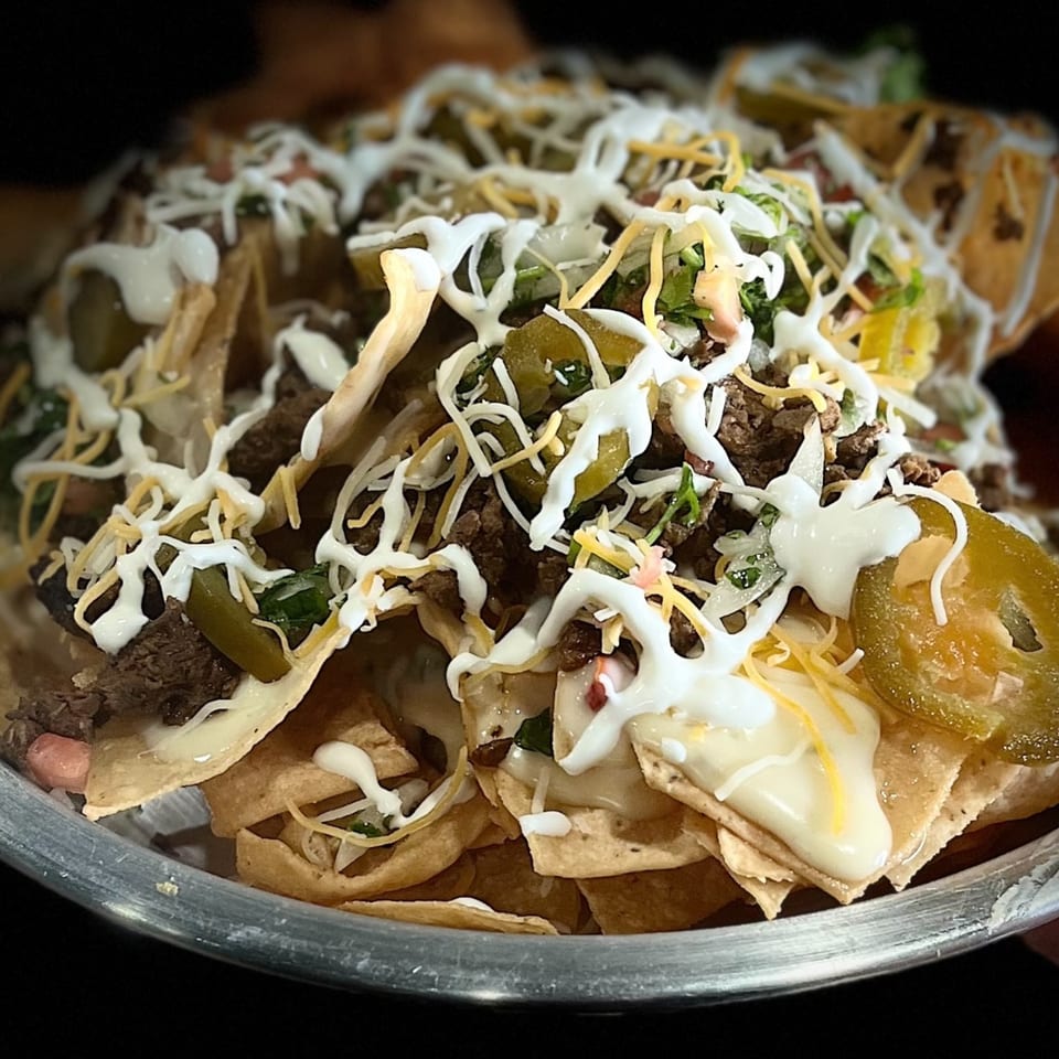 A close-up of loaded Mexican nachos with meat, cheese, jalapeños, and sour cream.